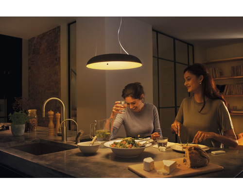 Twee vrouwen zitten in een keuken onder een hanglamp te eten.