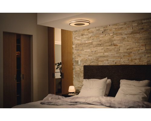 Slaapkamer met tweepersoonsbed, stenen muur en ronde plafondlamp