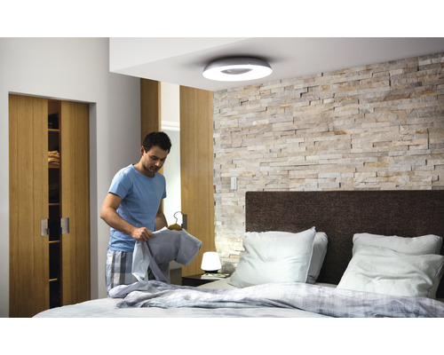 Slaapkamer met plafondlamp en man die een shirt vasthoudt