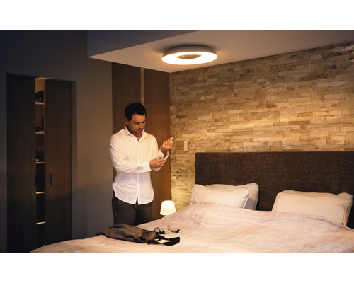 Lichte slaapkamer met plafondlamp, bed en man die zich aankleedt