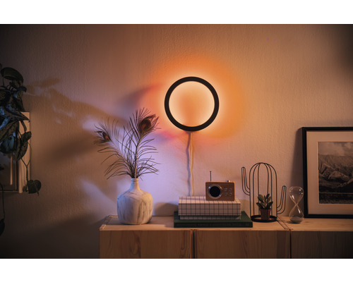 Woonkamer met cirkelvormige wandlamp, vaas met veren, radio en decoratiespullen op een houten kast.