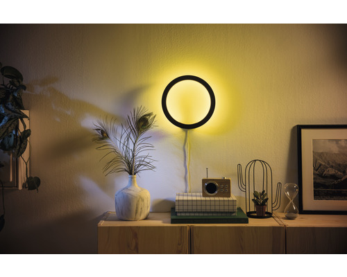 Woonkamerambiance met ronde wandlamp, decoratieve elementen en houten commode