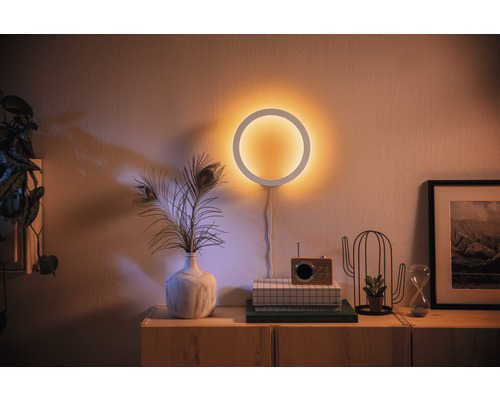 Decoratieve wandlamp in cirkelvorm boven een dressoir met decoraties.