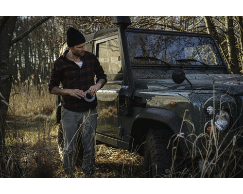 Man met tape naast een terreinwagen in het veld.