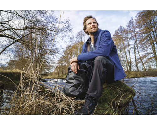 Een man zit met een rugzak aan de oever van een beek in de natuur.