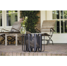 Metalen houtmand op een terras met tuinmeubelen op de achtergrond.