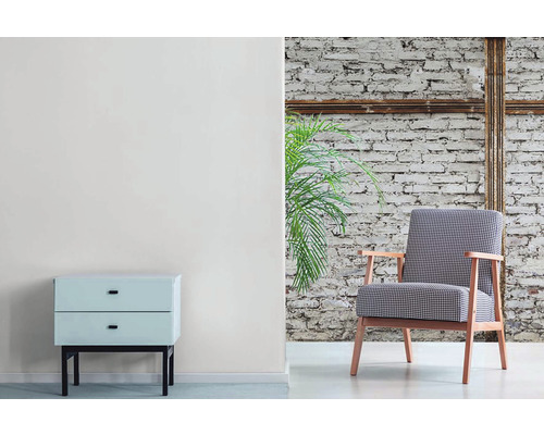 Woonkamer met fauteuil, nachtkastje en kamerplant voor een bakstenen muur