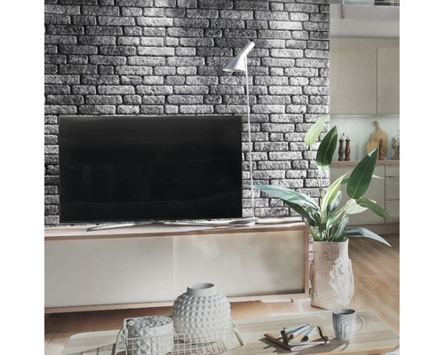 Woonkamer met gemetselde accentmuur, televisie, vloerlamp en decoratieve elementen op een salontafel