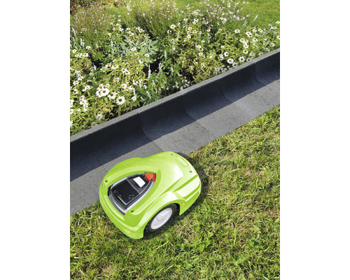 Groene robotmaaier op gazon naast een bloembedrand.