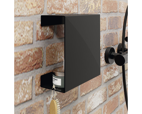 Zwarte doucherek aan een bakstenen muur met een borstel en een pot