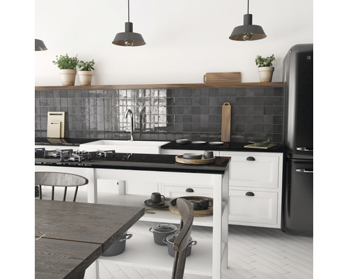 Lichte keuken met donkere tegels, kookeiland en zwarte apparaten.