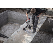 Een werknemer gebruikt een glaszuiger om een glazen paneel in een betonnen zwembad te plaatsen.