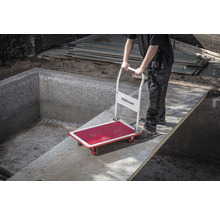 Een persoon vervoert een steekwagen over een betonnen voetbrug.