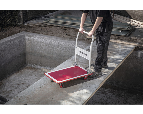 Een persoon vervoert een steekwagen over een betonnen voetbrug.