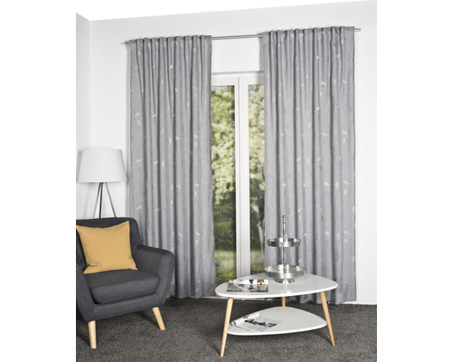 Woonkamer met grijze stoel, witte tafel en grijze gordijnen met patroon voor een raam