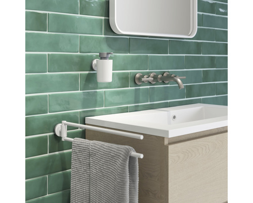 Badkamer wastafel met kraan, zeepdispenser en handdoekrek voor een groene muur.