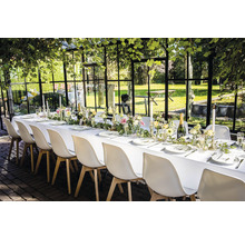 Feestelijk gedekte tafel met witte stoelen in een tuinhuis.