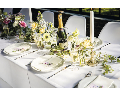 Gedekte tafel met borden, bestek, glazen, bloemen, kaarsen en een fles mousserende wijn voor een feestelijke gelegenheid