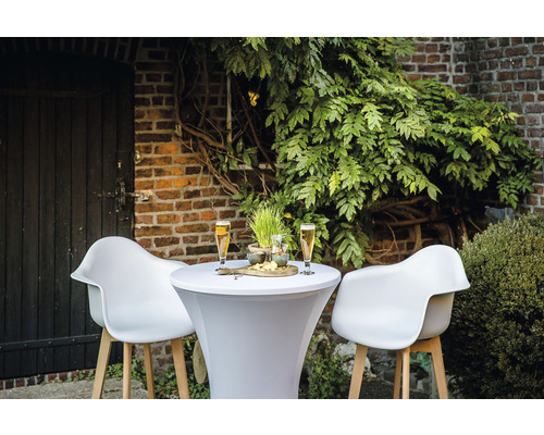 Buitenscène met een statafel, twee stoelen, drankjes en snacks voor een bakstenen muur en planten.