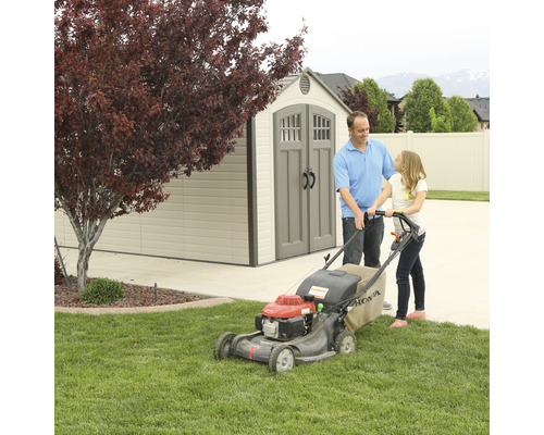 Vader en dochter maaien gazon met een grasmaaier voor een tuinhuis.