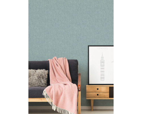 Woonkamer met patroonbehang, bank, kussen, deken en een klein kastje met een Londense afbeelding