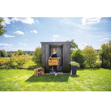 Vrouw draagt houten kist voor een metalen tuinhuis in de tuin.