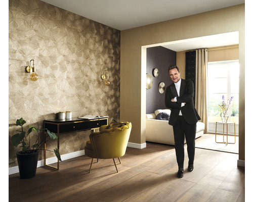 Woonkamer met patroonbehang, bureau, fauteuil en een persoon