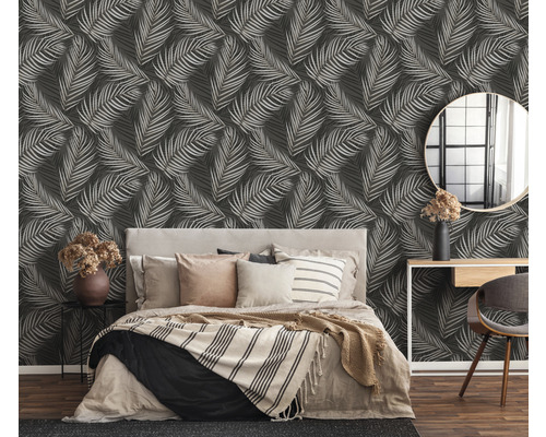 Slaapkamer met bed voor een wand met bladeren behang.