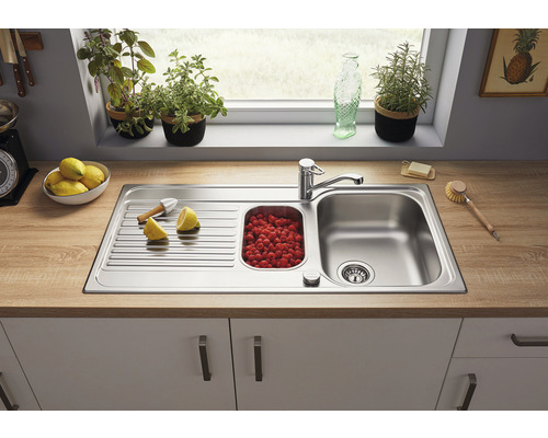 Roestvrijstalen spoelbak met afdruiprek en bak vol frambozen op een aanrecht
