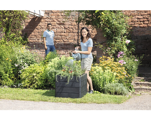 "Vrouw geeft planten water in een zwarte plantenbak in de tuin
