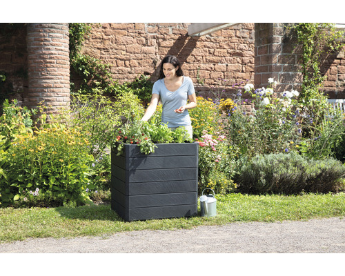 Vrouw tuiniert in een zwarte plantenbak in de tuin