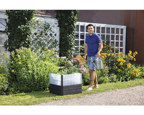 Verhoogde tuinbak met bloemen en man met gieter in de tuin