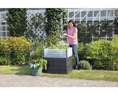 Vrouw geeft planten water in een kunststof plantenbak in de tuin.