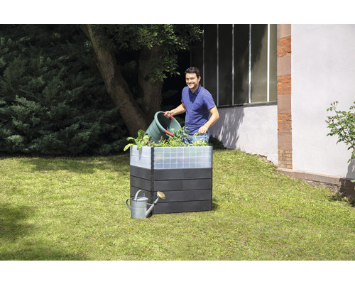 Houten plantenbak met een man die planten toevoegt, en een gieter in de tuin