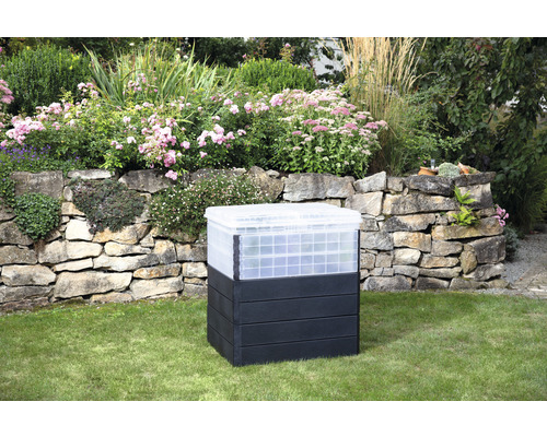 Kunststof compostbak in de tuin voor een stenen muur en bloembedden