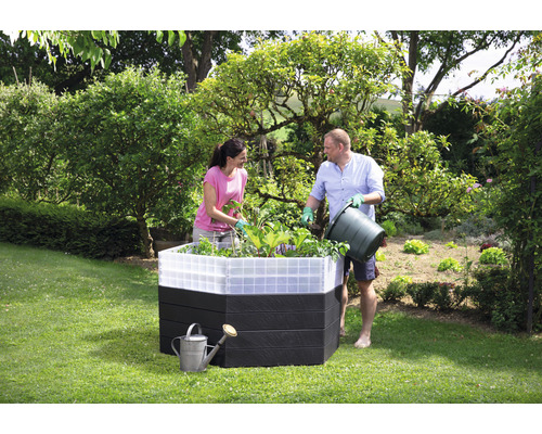 Mensen beplanten een verhoogde tuinbak in de tuin met een gieter ernaast.