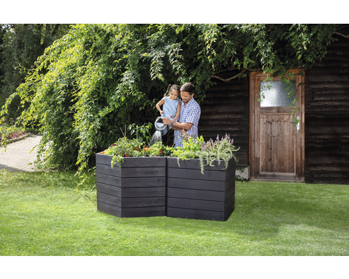 Een man en een kind geven planten water in een verhoogde tuinbak in de tuin.