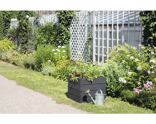 Tuinscene met beplante verhoogde tuinbak en gieter voor een tuinafsluiting