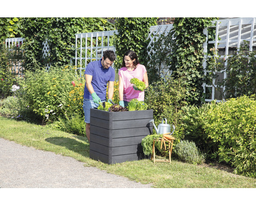 Een paar beplant een verhoogde tuinbak in de tuin.