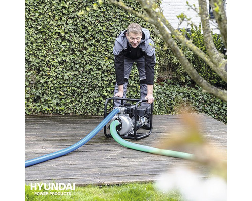 Man bedient een waterpomp van Hyundai in de tuin.