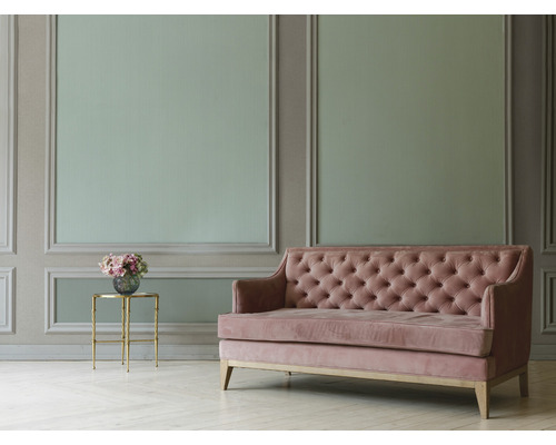 Gestoffeerde bank met knoopdetail naast een bijzettafel met bloemen voor een versierde muur