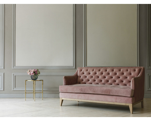 Woonkamer met grijs lambrisering aan de muur, sofa met knoopversiering en bijzettafel met bloemen