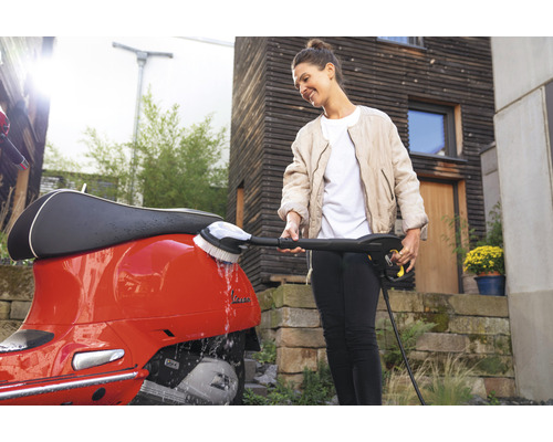 Vrouw reinigt rode scooter met borstel aan een hogedrukreiniger