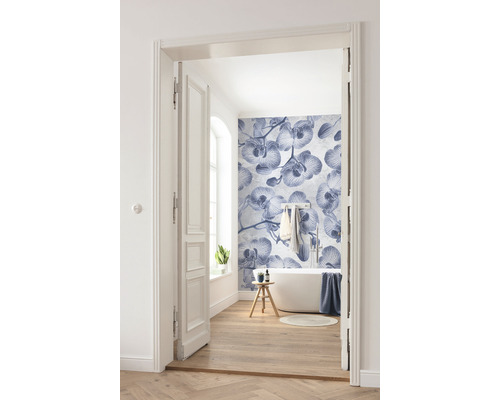 Lichte badkamer met ligbad, houten vloer en fotobehang met orchideeënpatroon, gefotografeerd door een open deur.