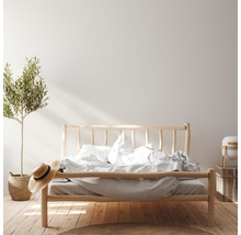 Lichte slaapkamer met houten bed, beddengoed, plant en strohoed.