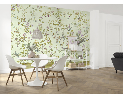 Een eetkamer met een behang met vogel- en bloemmotieven, een eettafel en stoelen.