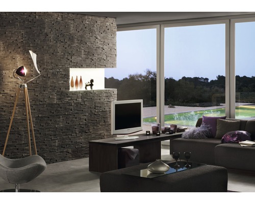 Woonkamer met stenen muur, televisie, lamp en raampartij met uitzicht op groen