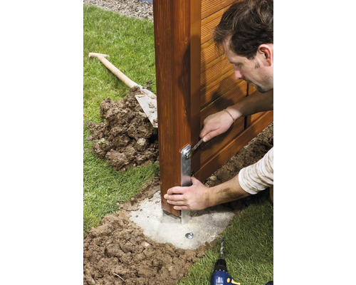 Man monteert hekpaal met steeksleutel op betonnen fundering in de tuin.