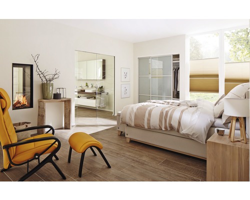 Lichte slaapkamer met bed, fauteuil, open haard en toegang tot de badkamer.