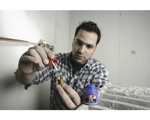 Een man brengt soldeerpasta aan op een messing fitting met een penseel. Een blik soldeerpasta staat op de voorgrond.